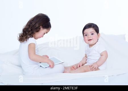 Baby girl (40 weeks) and her older sister (3.5 years) with tablet computer Stock Photo