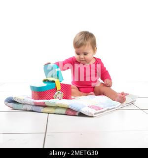 Baby girl (12 months) sitting on quilt playing with toy picnic basket Stock Photo