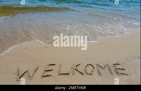Handwritting inscription welkome word on tropical sandy beach, travel concept card for holidays. Stock Photo