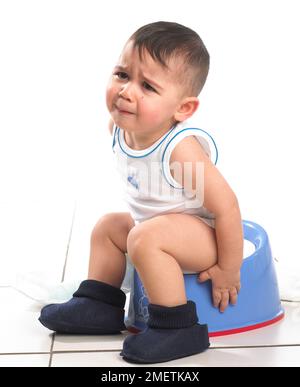 Boy wearing vest and slippers sitting on blue potty, 15 months Stock Photo