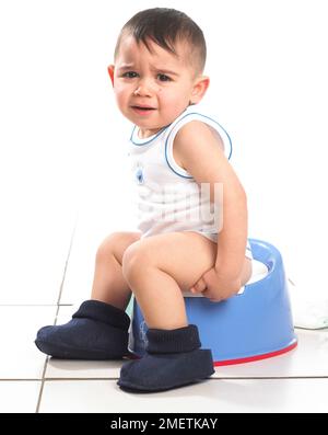 Boy wearing vest and slippers sitting on red car potty with steering ...