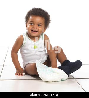Boy wearing vest and slippers sitting on floor, with nappy, 17 months Stock Photo