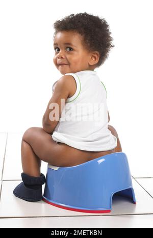 Boy wearing vest and slippers sitting on blue potty, 17 months Stock Photo