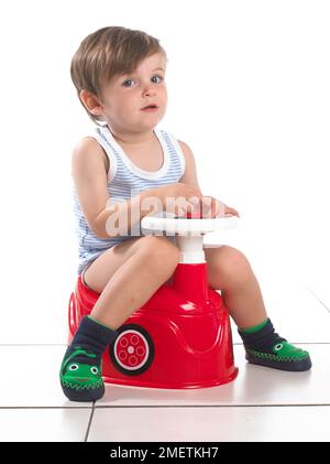 Boy sitting on a potty shaped as a car with steering wheel, 20 months Stock Photo