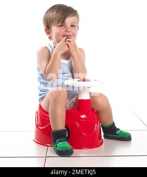 Boy sitting on a potty shaped as a car with steering wheel, 20 months Stock Photo