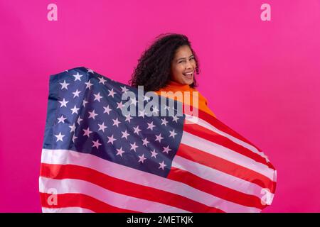 Curly-haired woman with the usa flag on a pink background, studio shot Stock Photo