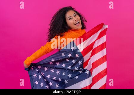 Curly-haired woman with the usa flag on a pink background, studio shot Stock Photo