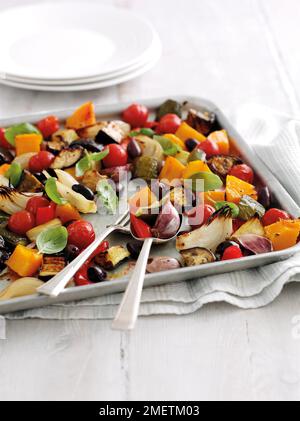 Roasted Mediterranean vegetables (courgettes, aubergines, onions, red peppers, butternut squash, garlic, cherry tomatoes), garnished with fresh basil leaves Stock Photo