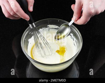 Making dressing for Caesar salad, stirring olive oil into mayonnaise mixture Stock Photo