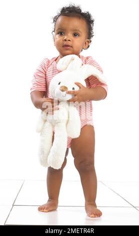 Girl standing holding toy rabbit, 18 months Stock Photo