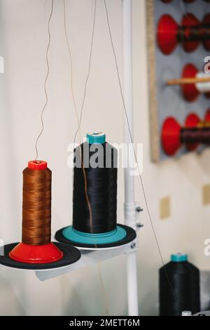 Spool of threads. Colorful thread spools hanging on fabric and textile industry manufacturing. Sewing machine on the table. Tailoring and small Stock Photo