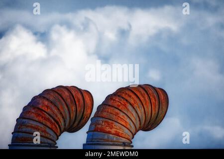 Rusty industrial air vents against a blue sky and fluffy cloud backdrop Stock Photo