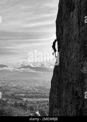 A grayscale vertical shot of a man's silhouette climbing the mountain of Gole del Melfa in Italy Stock Photo