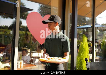 Restaurant staff holding a customer ordering a pizza on a sunny day wearing a hat at a cafe, Urth Caffe, Aramco Dahran, Saudi Arabia. Stock Photo