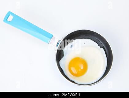 Egg being cooked in blue frying pan Stock Photo