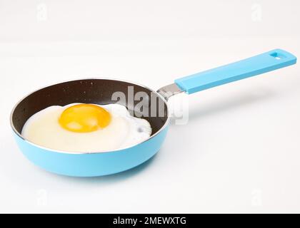 Egg being cooked in blue frying pan Stock Photo