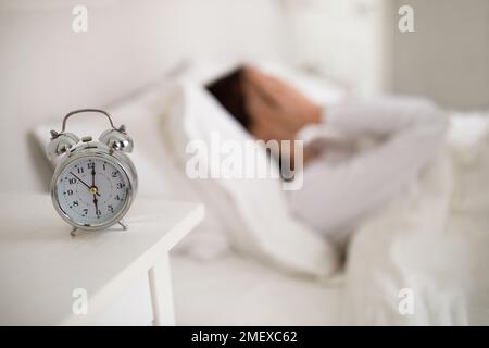Selective focus on alarm on bedside table over sleeping lady Stock Photo