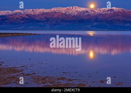 Reflections in Badwater Basin lake, Moonrise over Panamint Mountains and Badwater Basin, Death Valley National Park, California, USA Stock Photo