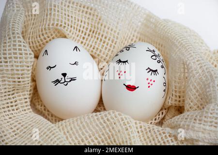 Close-up Two beautifully painted Easter eggs lie in an eco-friendly mesh bag on a white table. Funny faces are painted on the eggs. Copy space. Happy holidays Stock Photo