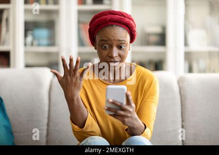 Stressed black woman holding smartphone, home interior Stock Photo