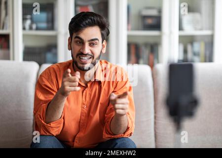 Arab guy vlogger streaming from home, using phone on tripod Stock Photo