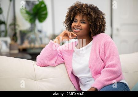 Dreamy cheerful african curly woman resting on couch at home Stock Photo