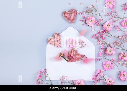 Spring floral composition made of fresh pink flowers,envelope and hearts on light pastel background. Festive flower concept. Flat lay, top view Stock Photo