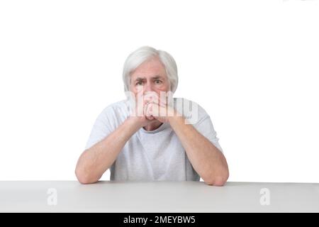 Horizontal shot of a worried white haired old man seated with his elbows leaning on the table.  White background.  Lots of copy space. Stock Photo