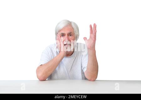 Horizontal shot of a distraught white haired man sitting at a table gesturing,  White background.  Lots of copy space. Stock Photo