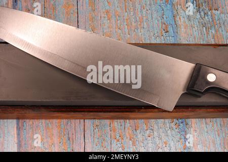 kitchen knife and sharpening stone on a wooden table Stock Photo