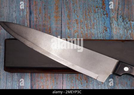steel knife resting on a sharpening stone with a rustic wooden background Stock Photo