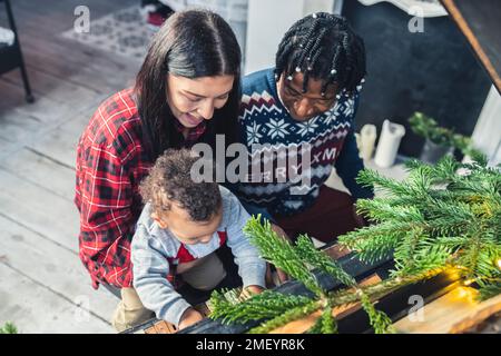 Multiracial parents and their child son playing piano under the Christmas tree. High quality photo Stock Photo