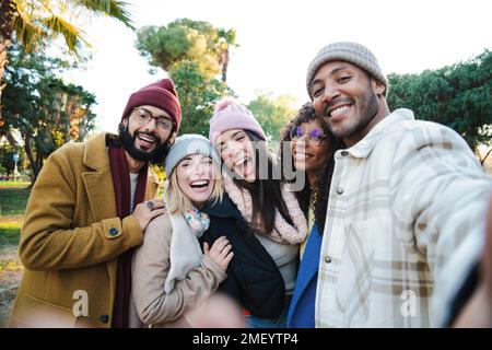 Group of young friends having fun taking a selfie portrait with a smartphone in a park, smiling happy people laughing taking a photo looking at camera outdoors in autumnal season. Tourism concept. High quality photo Stock Photo