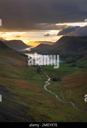 View of Buttermere and Crummock Water taken from high up in mountains with golden sunlight breaking through dark clouds. Lake District, UK. Stock Photo