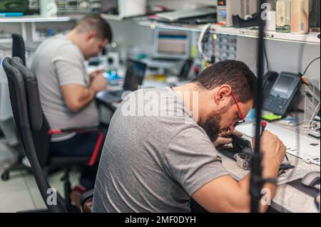 The employees in the workshop do their daily work. A workbench full of various tools and items needed to repair electrical appliances Stock Photo