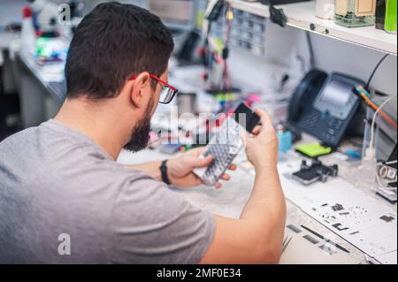 The employees in the workshop do their daily work. A workbench full of various tools and items needed to repair electrical appliances Stock Photo