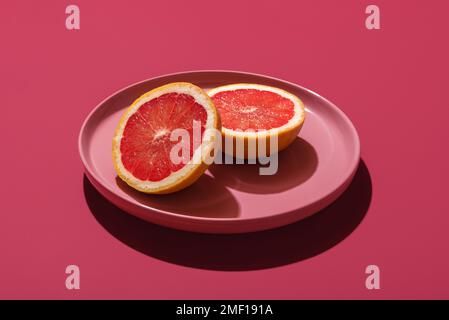 Grapefruit sliced in half on a pink plate in bright light. Plate with a grapefruit minimalist on a magenta background Stock Photo