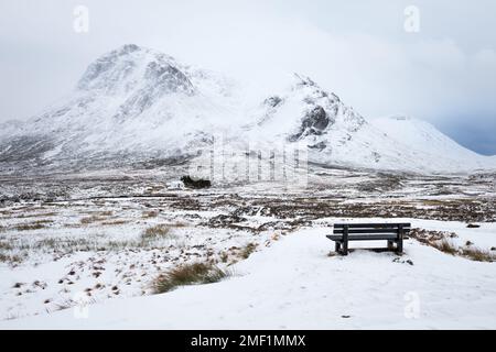 Winter afternoon view of wooden bench looking over Glencoe with snow covered mountains. Scottish Highlands, UK. Stock Photo