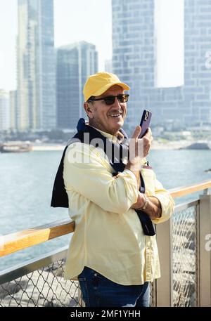 Happy senior man using smartphone along promenade next to marina. Stock Photo