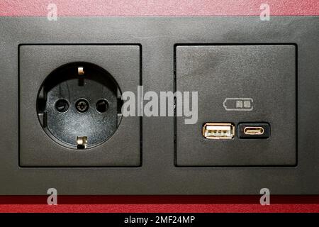 A modern black 220V, USB and USB C socket block is built into the wall surface Stock Photo