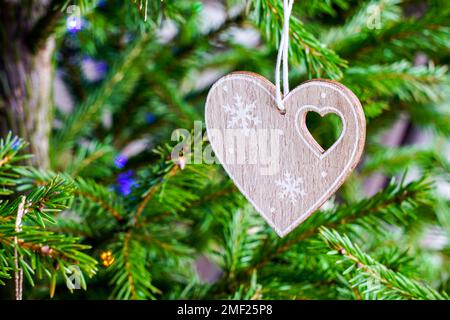 A miniature wooden heart with a small heart-shaped cutout and a snowflake decoration hangs on the Christmas tree Stock Photo