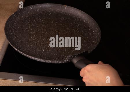 photo of an empty frying pan in hand on an empty stove Stock Photo
