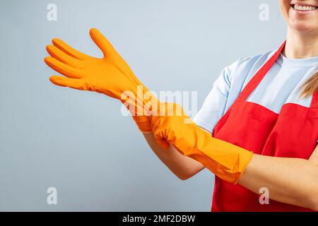 A woman in red apron putting on protective gloves on blue background Stock Photo