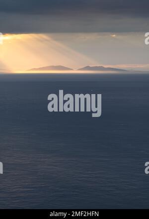 Beautiful rays of sunlight shining through dark clouds over Scottish Outer Hebrides in the far distance. Isle of Harris, Scotland, UK. Stock Photo