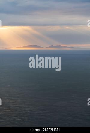 Beautiful rays of sunlight shining through dark clouds over Scottish Outer Hebrides in the far distance. Isle of Harris, Scotland, UK. Stock Photo