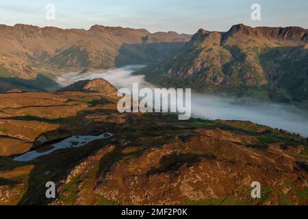 Aerial view of mist in valley on a sunny morning. Langdale Pikes from above Lingmoor Fell, Lake District, UK. Stock Photo