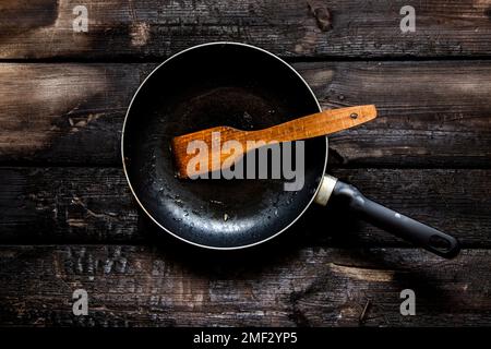 dirty frying pan after frying on an old wooden table in the kitchen, non-stick frying pan after eating, kitchen utensils Stock Photo