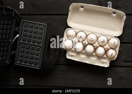 chicken eggs in boxes and text 2022 on eggs and waffle iron, happy new year 2022, chicken eggs on the table, 2021 and 2022 Stock Photo