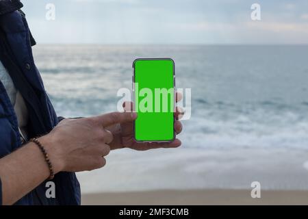 hands of a man pointing his finger at a mobile phone with a blank green screen Stock Photo