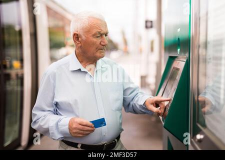 Senior man using ATM machine while standing on tram station Stock Photo